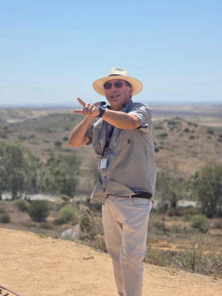 Pepe Heiblum guiding a group in the field, with the Gaza border landscape behind him